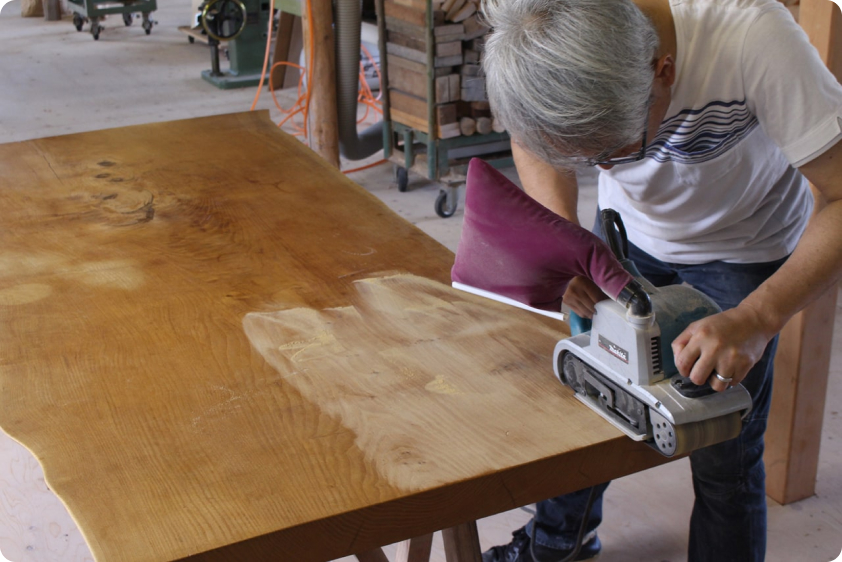 一枚板を丁寧に研磨するヒダコレ家具工房のスタッフ